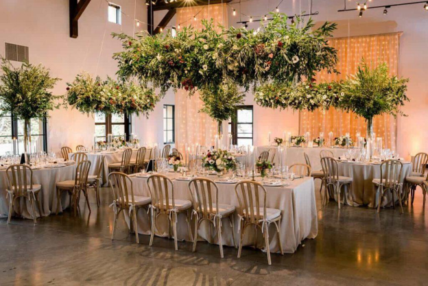Chairs and tables decorated with floral arrangements in a room set up with fabric, floral arrangements and fairy lights