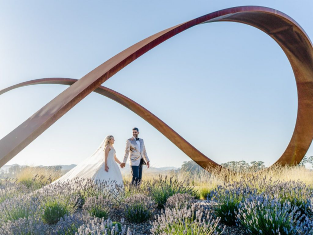 A bride and groom stand among fields of lavender under a structure resembling an infinity sign making it one of the most romantic wedding destinations in the U.S.