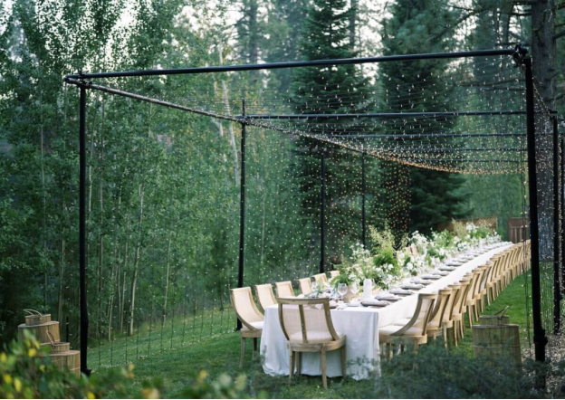 A dining table set under a canopy of fairy lights by coniferous trees shows just how any location can be transformed into a romantic wedding destination.