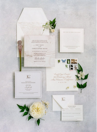 A flat lay of a wedding invitation suite with floral accents, RSVP card, and elegant calligraphy, showcasing a sophisticated wedding design.
