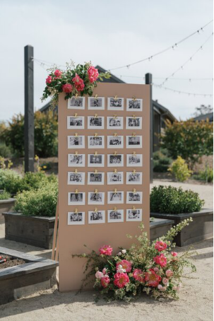Outdoor wedding photo display board decorated with fresh pink flowers, showcasing black-and-white photos for a sentimental touch.