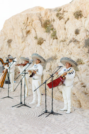 A mariachi band dressed in traditional attire performing at an outdoor rehearsal dinner with rocky surroundings.