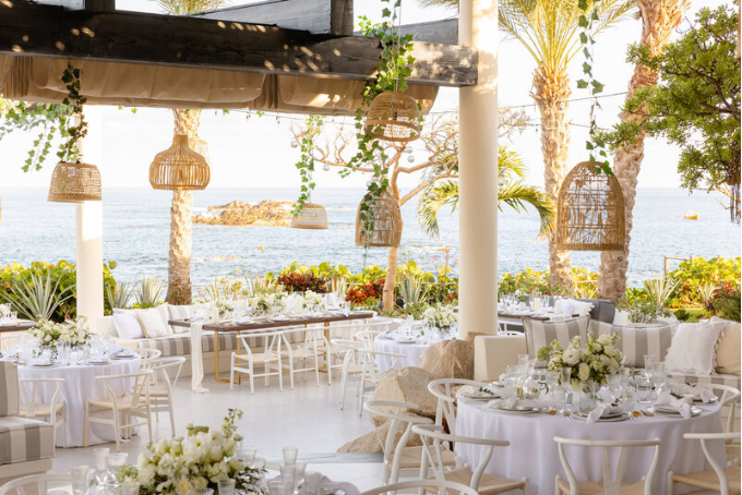 Rehearsal dinner venue by the sea, decorated with white floral arrangements, wooden details, and wicker lanterns for a tropical ambiance.