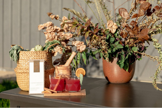 Two drinks sit on a tray by a woven basked and autumnal dried flower décor on a tabletop