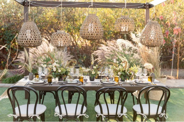 An outdoor table setup with floral décor and boho chic elements with cane lanterns hanging overhead