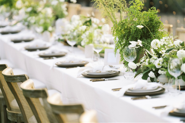 A beautifully styled table with white linens, elegant tableware, and green floral arrangements.