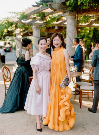 Two wedding guests posing in stylish dresses, one in soft pink and the other in vibrant orange, against an elegant outdoor backdrop.