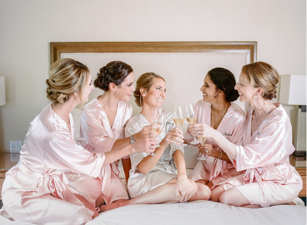 Bride and bridesmaids in pink satin robes sharing a toast, symbolizing the joy and anticipation before the wedding ceremony.