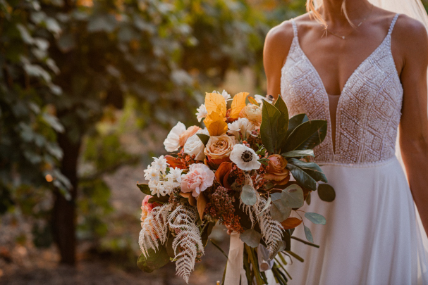 A bride in her wedding dress is standing outdoors with a bouquet of flowers