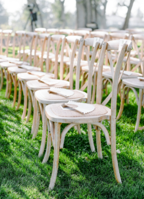 A group of chairs placed outdoors for a wedding ceremony with fans on each chair