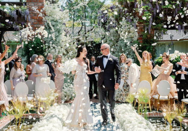 A stunning couple walks down a flower-adorned aisle as guests shower them with petals