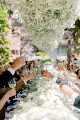 Guests raising glasses in a beautifully decorated outdoor reception with hanging floral arrangements