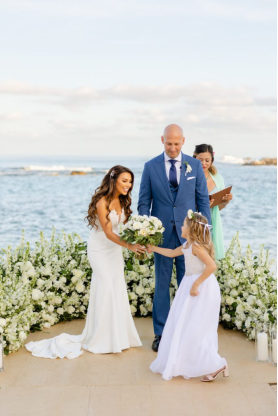 Bride and groom sharing a sweet moment with their flower girl at a seaside wedding altar
