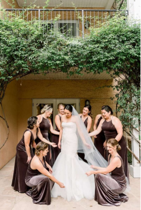 Bride surrounded by her bridesmaids adjusting her veil in an elegant outdoor setting.
