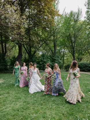 Bridal party walking in a lush green garden, wearing vibrant floral dresses