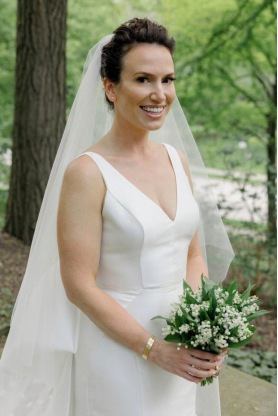Bride in a minimalist white gown holding a delicate bouquet of lilies of the valley in an outdoor setting