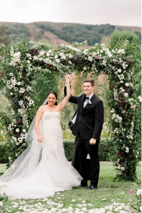 A happy couple celebrates their wedding under a lush floral arch in an outdoor luxury ceremony
