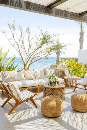 An outdoor wedding lounge setup with natural wooden furniture and a scenic ocean backdrop