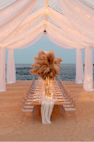 Stylish beachfront wedding seating arrangement with flowing linens and a scenic ocean backdrop in Los Cabos