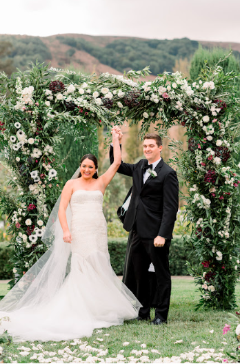 A newlywed couple walking down the aisle at a coastal wedding, surrounded by floral arrangements and guests