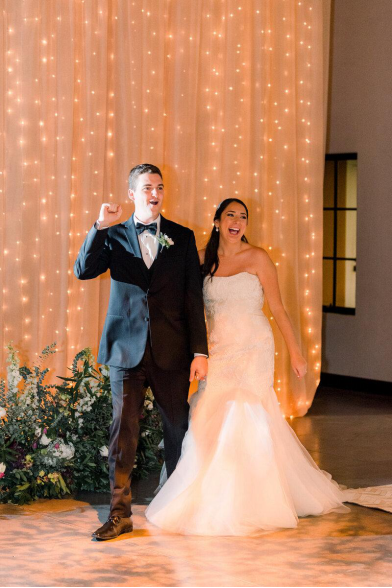 Newlywed couple making a joyful entrance, hand in hand, surrounded by soft lighting and décor