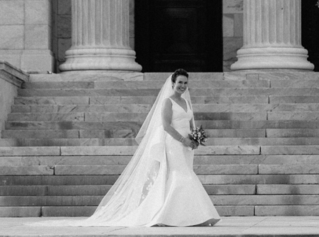 A bride in a simple and elegant gown standing in a softly lit room.