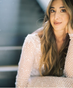 A woman with clear, radiant skin and long, wavy hair looks directly at the camera