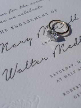Diamond engagement ring placed on elegant wedding invitation with scripted names