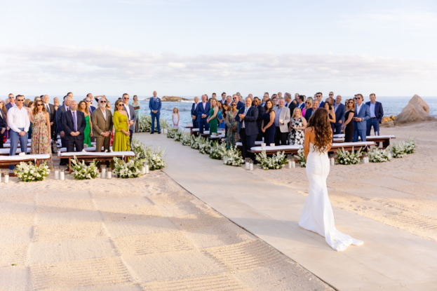 Bride walking down the aisle at an elegant beach wedding ceremony in Cabo, with guests standing