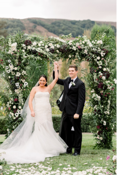An image of a bride and groom standing under a floral arch
