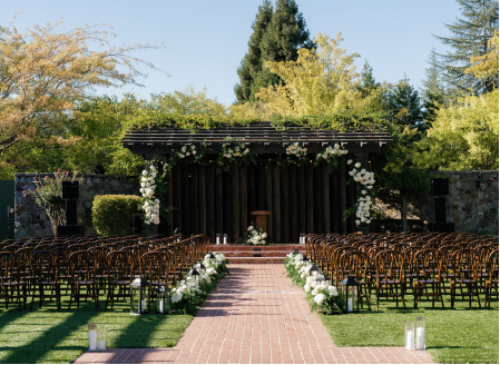 Outdoor wedding ceremony space in Charlotte featuring dark wood chairs, floral aisle arrangements, and a pergola with white rose decorations.