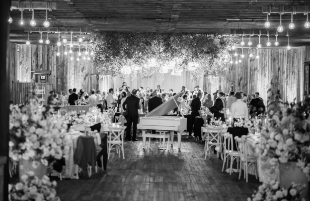 Black and white photo of a large wedding reception with a white grand piano as the centerpiece