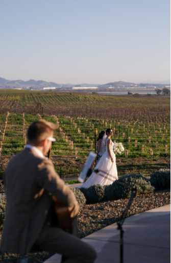 Bride walking down the aisle in a Napa Valley vineyard wedding as a guitarist performs in the background