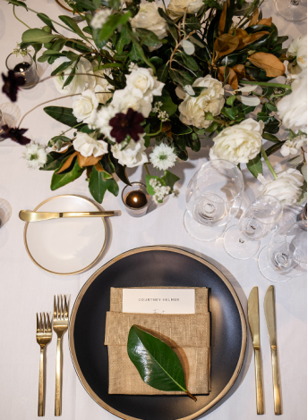 Sophisticated wedding table setting with black plate, gold cutlery, floral centerpiece, and personalized name card