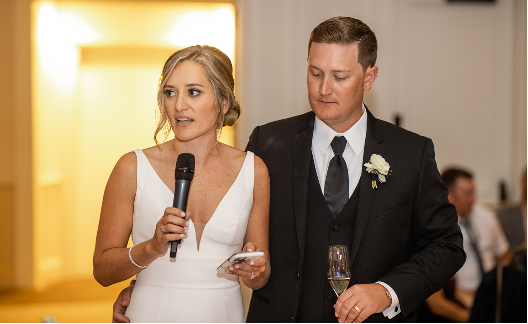 Bride and groom sharing a thank-you speech at their wedding reception with champagne in hand.