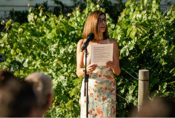 A wedding guest reading from a script during an outdoor ceremony with greenery backdrop