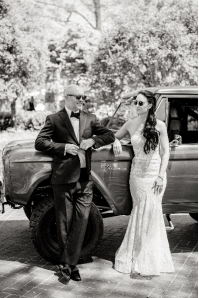 An image of a bride and groom posing against a car