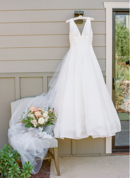 a sleeveless white wedding gown hung outside with a bouquet